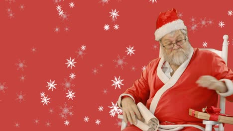 snowflakes falling over santa claus holding christmas presents against red background