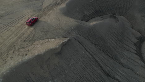 Dramatic-Drone-Shot-of-Red-SUV-Vehicle-Moving-on-Dirt-Road-and-Hill-in-Desert-Landscape-of-Utah-USA