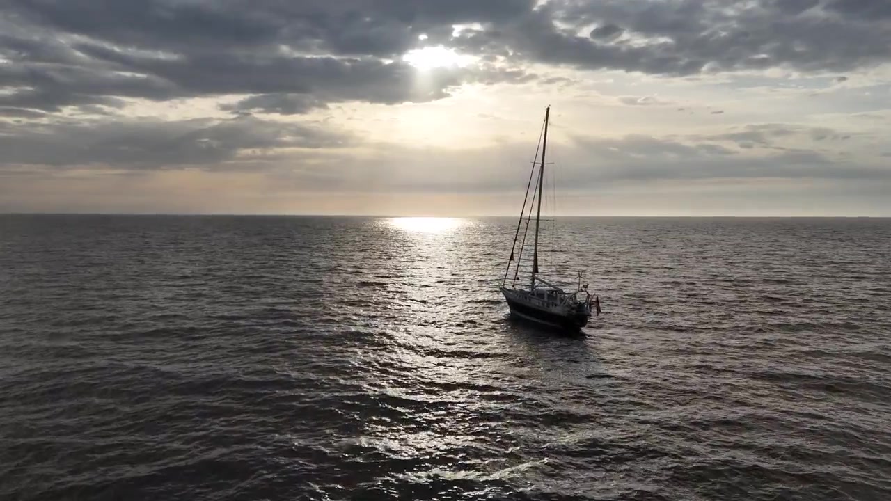 Drone si avvicina da vicino a una barca a vela solitaria su un mare calmo alla calda luce del tramonto