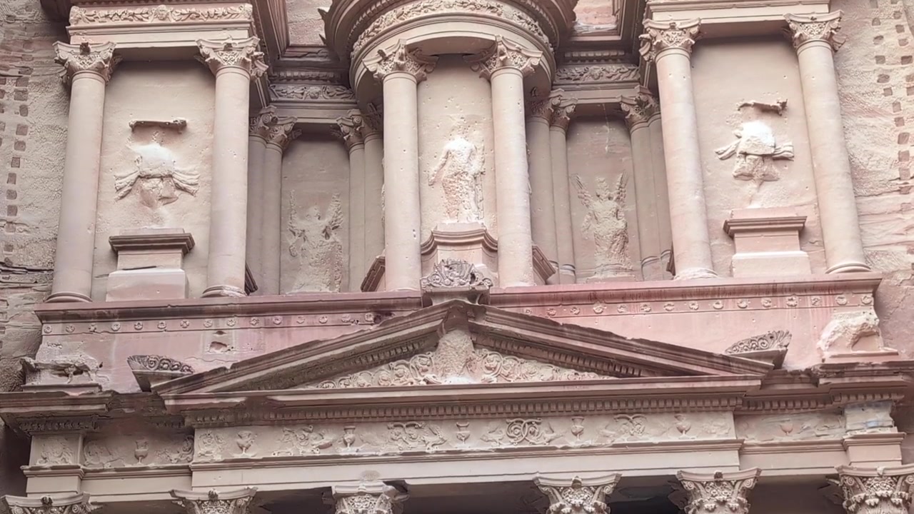 Riprese ravvicinate con panoramica verso il basso dell'ingresso del Tesoro di Petra, scavato nelle scogliere di arenaria in Giordania. Vista dettagliata dell'architettura nabatea, colonne, intagli e antica muratura.