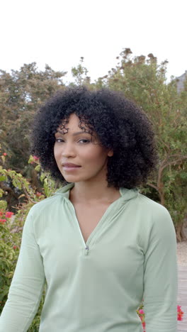 vertical video: smiling woman in green top standing outdoors in garden setting