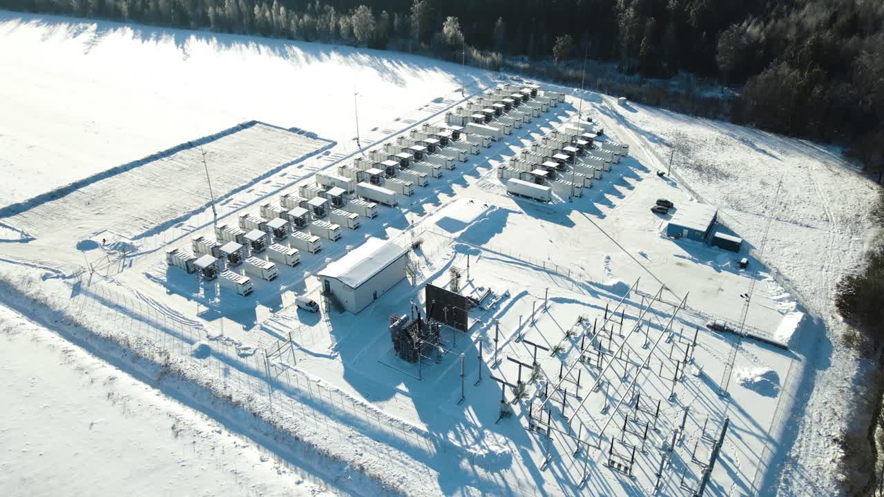 Široký zimní letecký záběr odhaluje největší estonské velkokapacitní úložiště pro energetickou síť, s kontejnerovými jednotkami vrhajícími dlouhé stíny na čerstvý sníh a lesní okolí.
