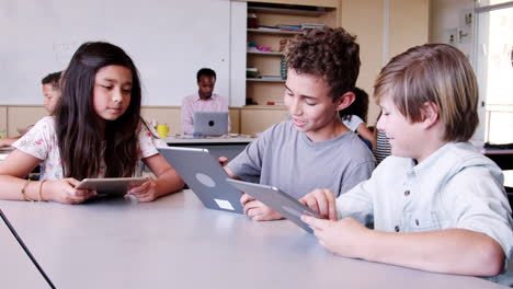 tres niños usando computadoras tablet en clase de escuela primaria