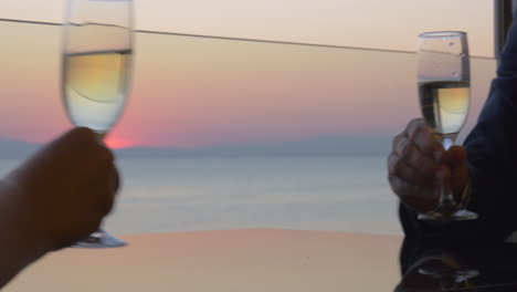 woman and man hands are clinking glasses of champagne on sunset sea background close up view