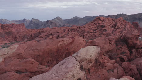 Beautiful-aerial-wide-shot-of-the-Red-Sandstone-in-Nevada-revealing-the-vast-landscape-and-mountains