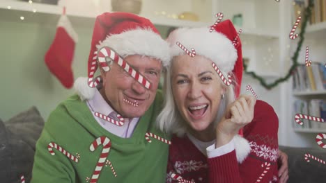 Animation-of-candy-canes-over-senior-caucasian-couple-having-video-call-with-christmas-santa-hats