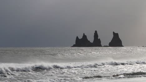 mares agitados que llegan a la orilla en reynisfjara playa de arena negra con grandes pilas de basalto en el fondo