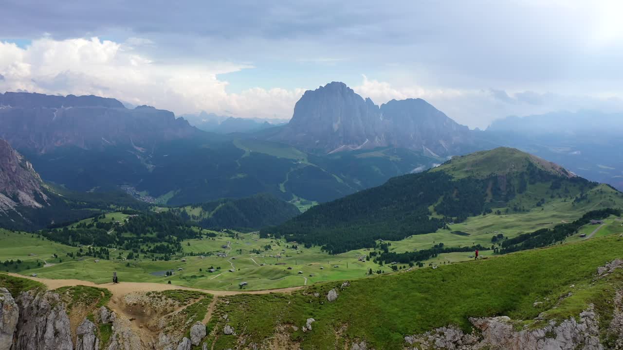 Male running down Seceda mountain ridge with Val Gardena backdrop, forward aerial