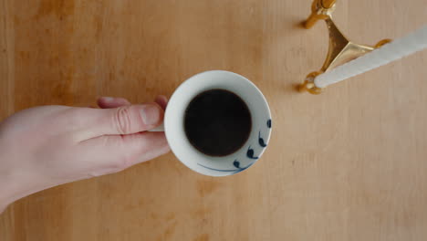 Person-picking-up-a-full-cup-of-hot-coffee-from-wooden-table