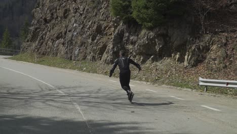 a skater in full black protective gear descends a mountain road at thrilling speed, then brakes to a stop.