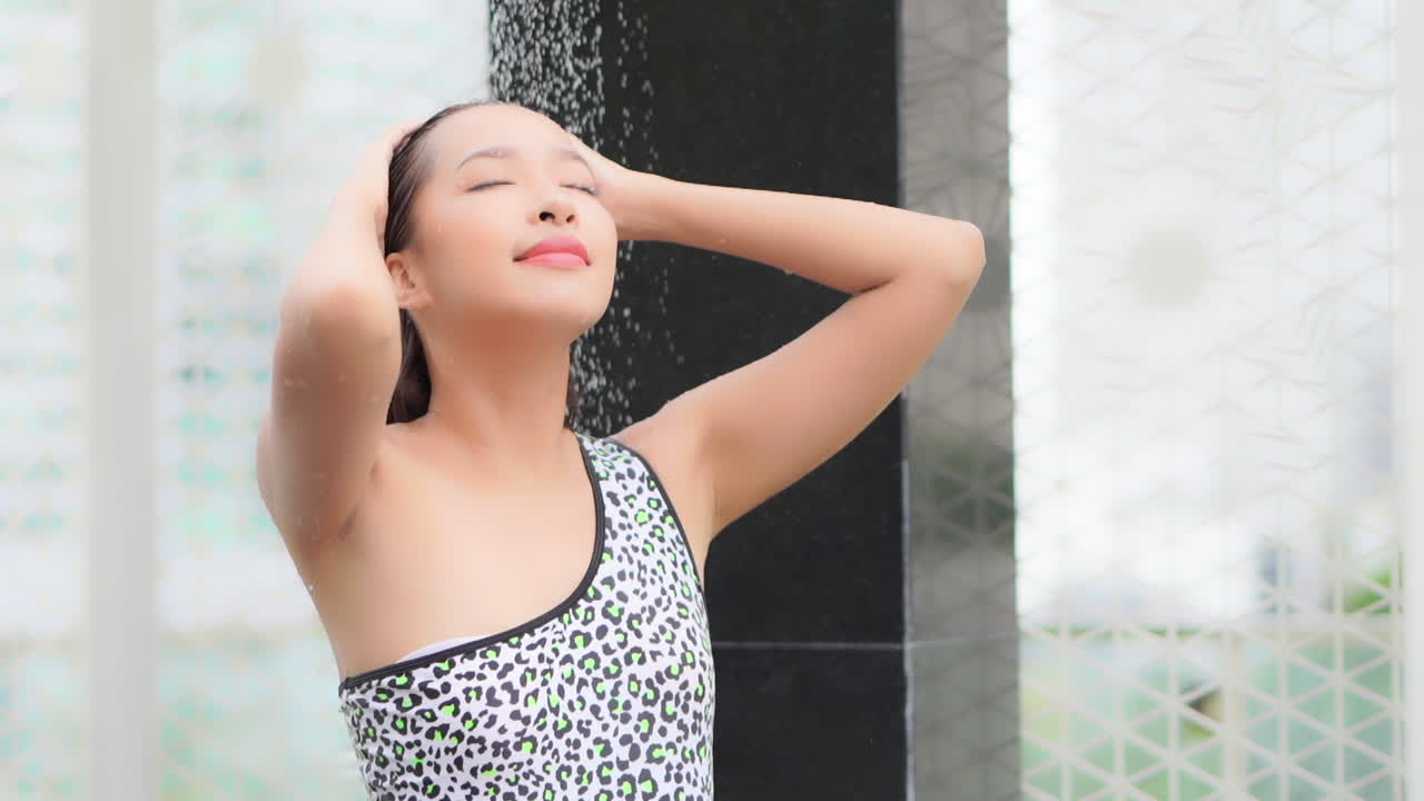 샤워실에 서서 수영복을 입은 젊은 매력적인 여성이 수영장에서 염소를 씻어낸다