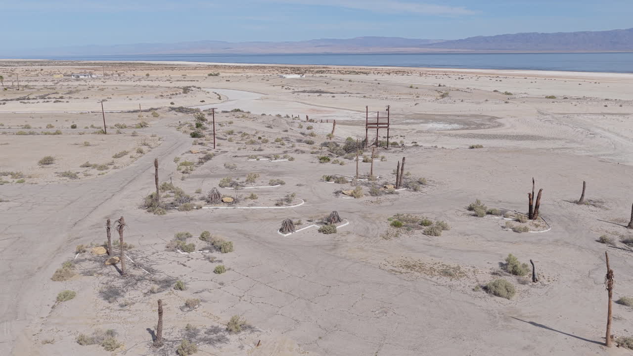 Drone shot arcing left to right above the abandoned site of the former Salton Bay Yacht Club in Salton City, California with the Salton Sea visible in the background