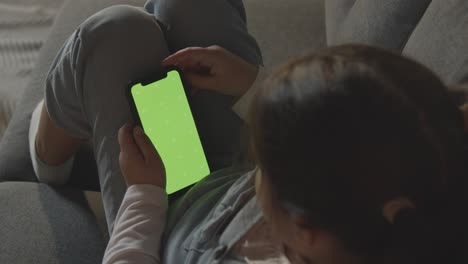 Young-Girl-At-Home-Relaxing-On-Sofa-Looking-At-Green-Screen-Mobile-Phone