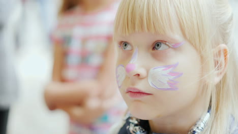 the child is applied with aquagrim tassel draws a cat mask concept - children's holiday