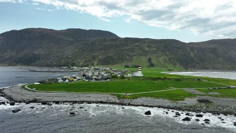 Alnes-lighthouse-on-idyllic-coastal-peninsula-in-Norway---Backward-moving-aerial-above-ocean-revealing-full-panoramic-view-of-lighthouse-and-the-small-town