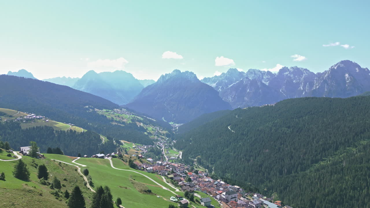 video de drones volando hacia la cordillera de los dolomitas en verano sobrevolando una ciudad histórica en la ladera rodeada de bosques y tierras de cultivo