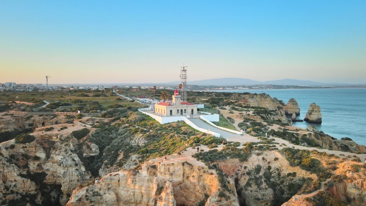 Camera spirals around Ponta da Piedade lighthouse, capturing rugged cliffs, coastal trails, and sweeping Atlantic views under the clear Algarve sky