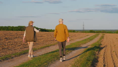 two people walking down a country road through a field at sunset