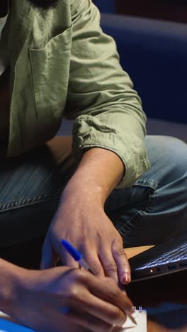 Vertical Video Black freelancer taking notes on his textbook in order to solve his tasks