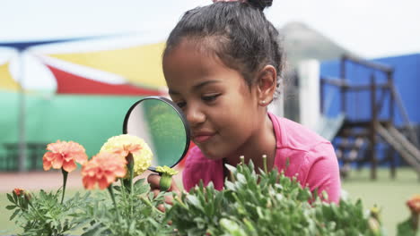 in a school garden, a young biracial student examines flowers with a magnifying glass