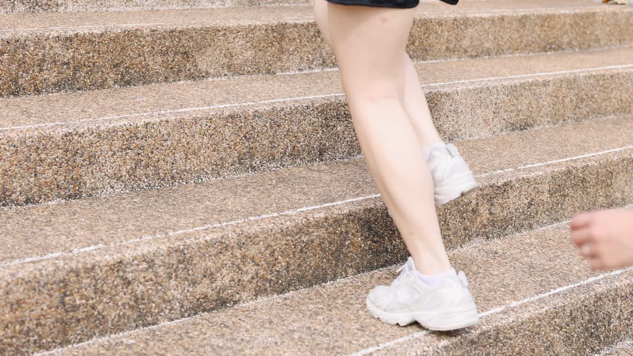 Una donna con scarpe da ginnastica bianche sale scale di cemento durante un allenamento all'aperto in pieno giorno