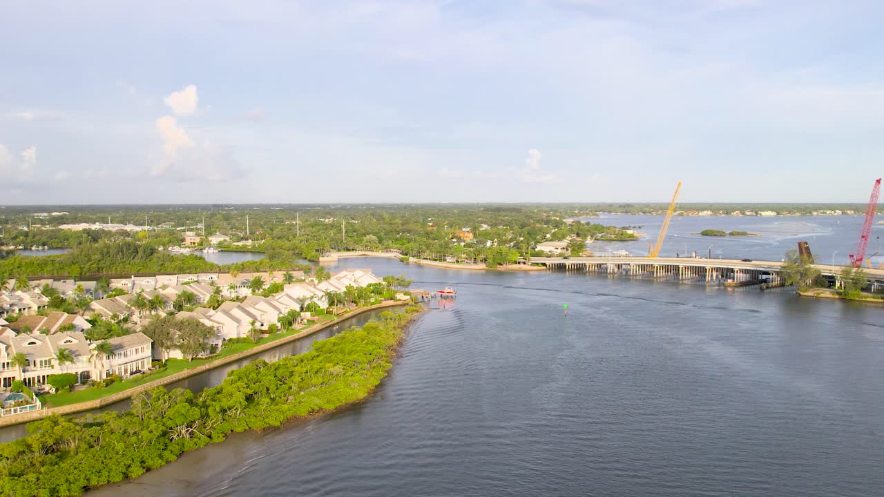 A drone captures a sweeping aerial view of a river winding through a developed cityscape, with bridges and green spaces lining the waterfront