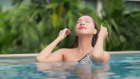 Toma-De-Belleza,-Mujer-Asiática-Tocando-El-Cabello-Y-Alisando-El-Cabello-En-La-Piscina-En-Un-Día-Soleado,-Vista-Frontal-En-Cámara-Lenta-De-Primer-Plano