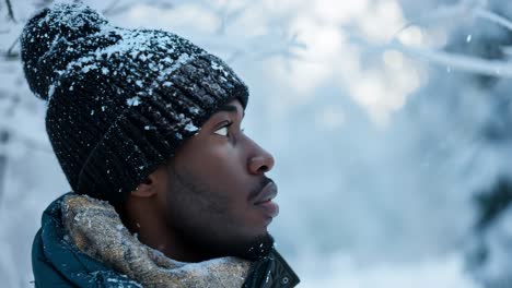 close up portrait of a young black man wearing a wool hat and a scarf while enjoying a snowfall in a forest during winter, snowflakes falling on his face