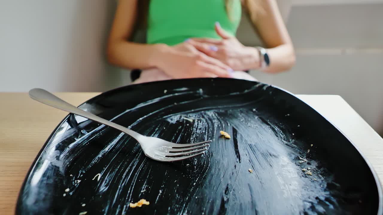 Overeating aftermath as green top woman clutches belly behind scraped clean plate
