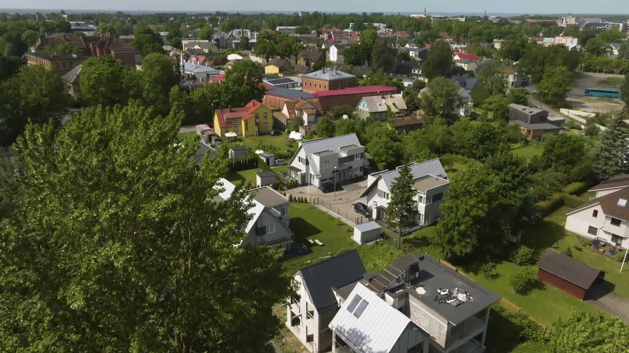 Drone tilting over trees, revealing a community of homes, summer day in Estonia
