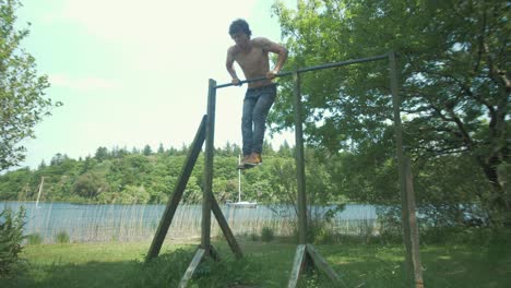 a young topless man performs muscle up exercise in nature