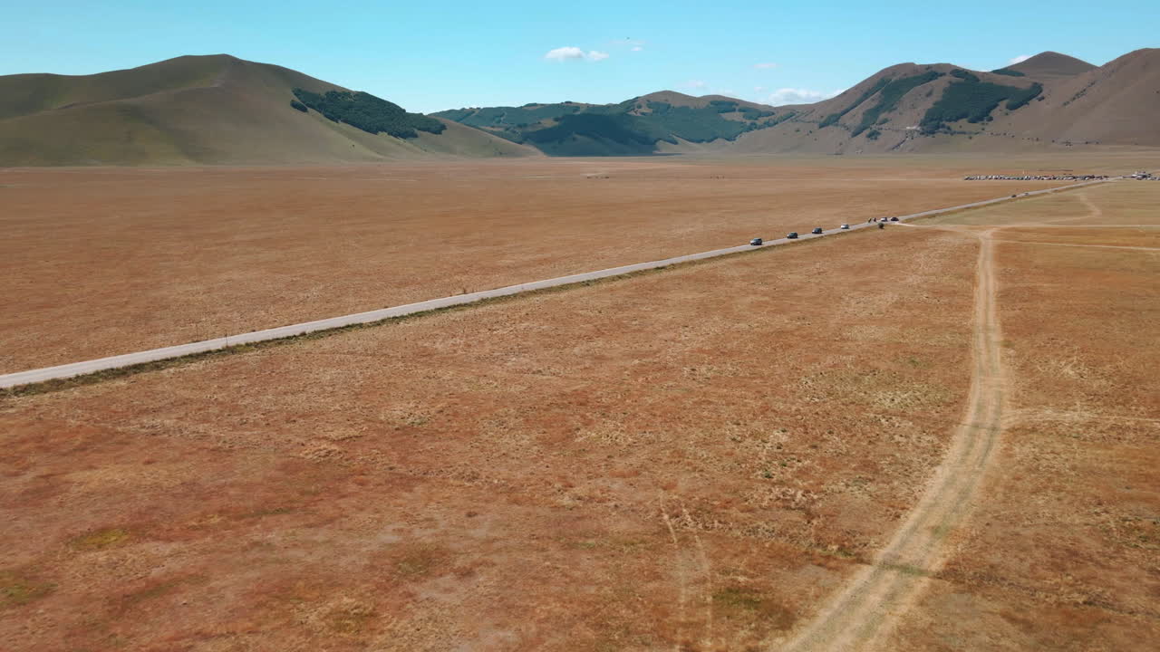 이탈리아 토스카나주 노르시아의 카스텔루치오 근처 화창한 날 도로에서 운전하는 차량과 함께 피아나 그란데 상공을 비행하는 드론