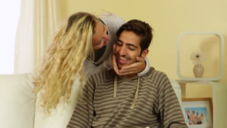 man reading a book while his girlfriend runs up behind him on the couch