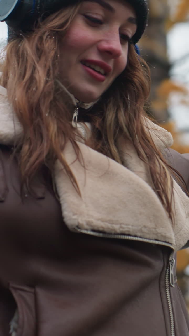 Close view of smiling young girl wearing black knit cap, brown shearling jacket with arms outstretched, walking joyfully outdoors on cool autumn day, embracing nature and fresh air