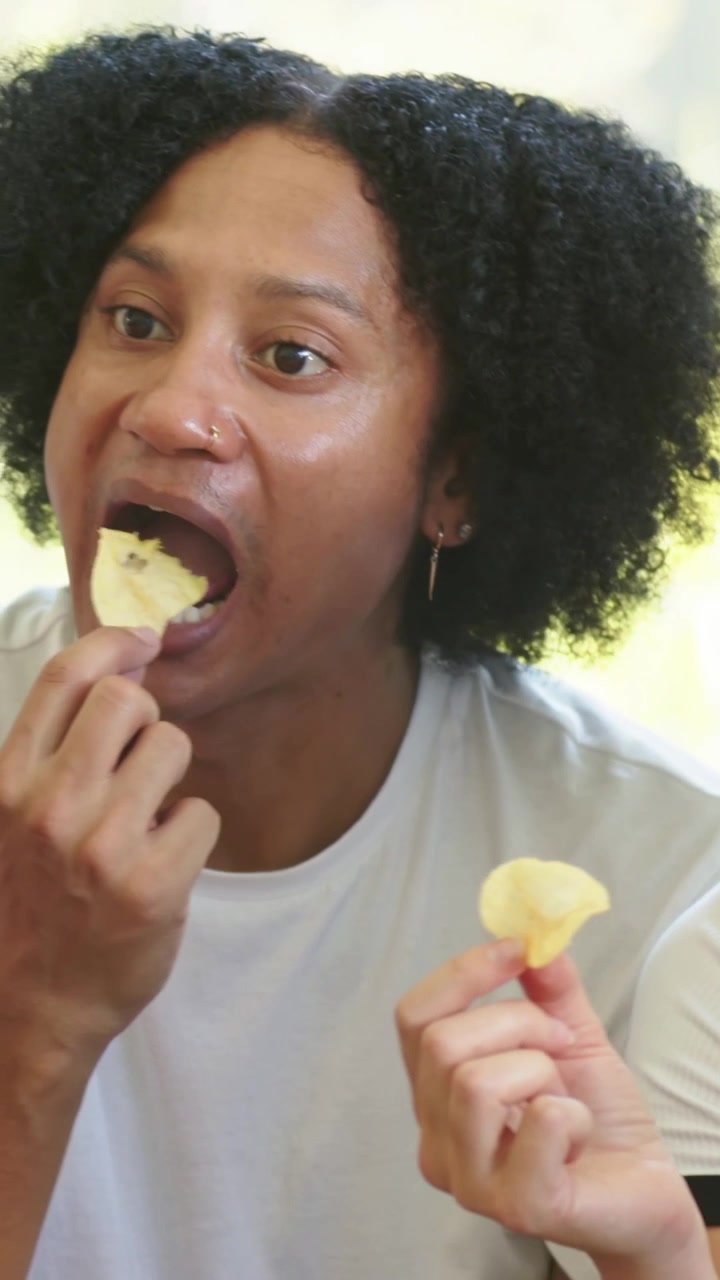 Vidéo verticale : Femme en polo blanc et homme tendant la main et partageant des chips sur un canapé, tenant un verre.