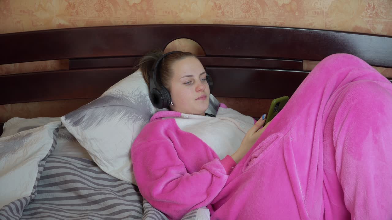 chica en pijama en una cama con auriculares está hablando en una llamada de video en el teléfono