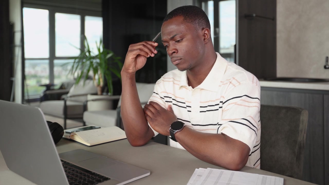 Thoughtful Young African American Man Working on Laptop at Home