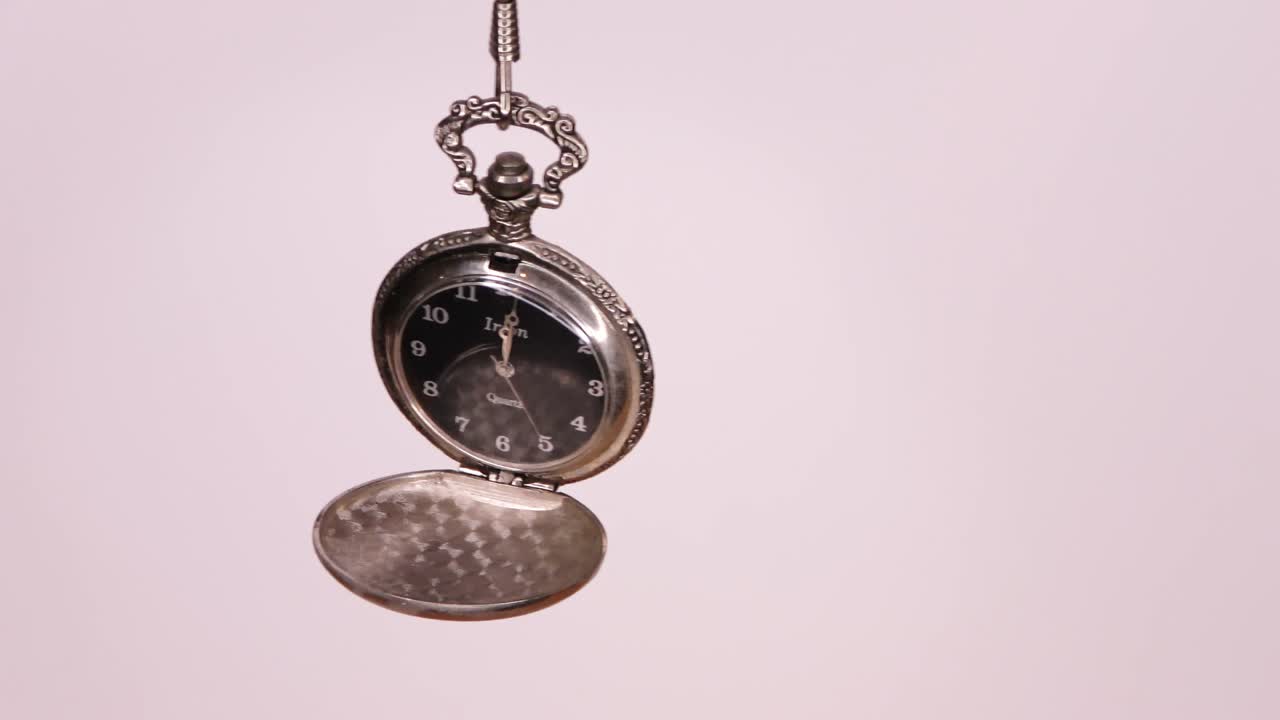 An old opened pocket watch on a silver chain swings slowly back and forth.