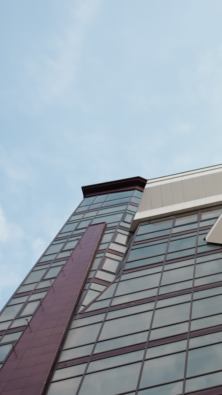 Close view of a modern city building with a sleek glass facade and architectural design, the upward perspective highlights the building's structure against a backdrop of a clear blue sky