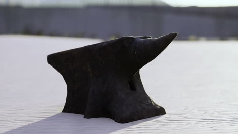 unique black anvil resting on sunlit sandy shore at midday