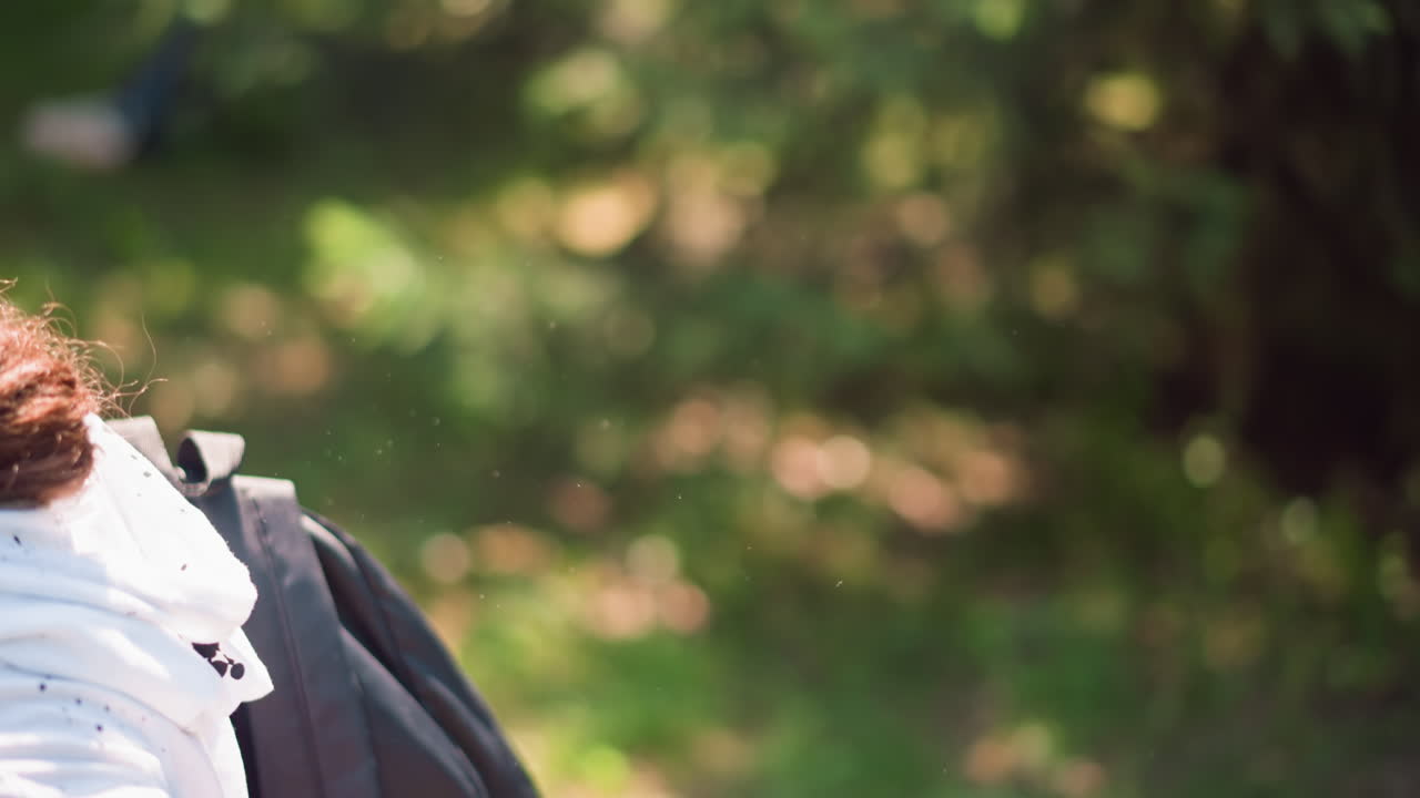 붉은 챙 모자와 백팩을 메고 그늘진 오솔길에서 미소짓는 젊은 등산객, 나뭇잎이 무성한 길을 걸으며 몸을 앞으로 기울여 땅을 살피고, 고개를 돌려 소리를 듣고, 편안하게 웃는 모습