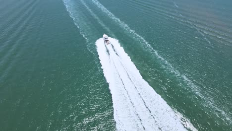 aerial drone shot of a boat seen from above following other boats in the ocean near the beach with a mountainous horizon