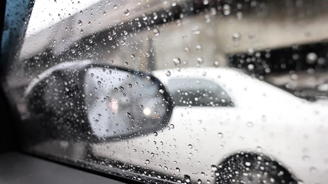 Raindrops on car window, blurred white car passing, overcast daylight, urban Bangkok street scene
