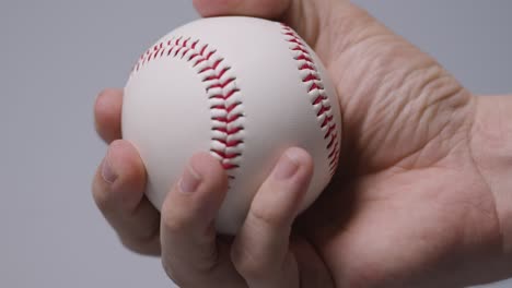 Primer-Plano-De-Mano-Lanzando-Y-Atrapando-Una-Pelota-De-Béisbol-Contra-Un-Fondo-Gris