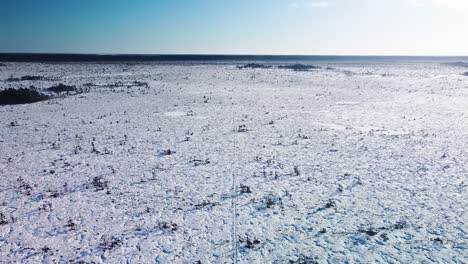 aerial birdseye view of snowy bog landscape with hiking trail and frozen lakes in sunny winter day, dunika peat bog , wide angle descending drone shot