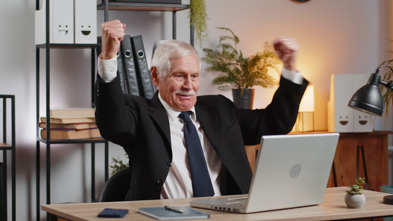 Senior happy caucasian businessman working on laptop shocked by sudden victory at home office desk