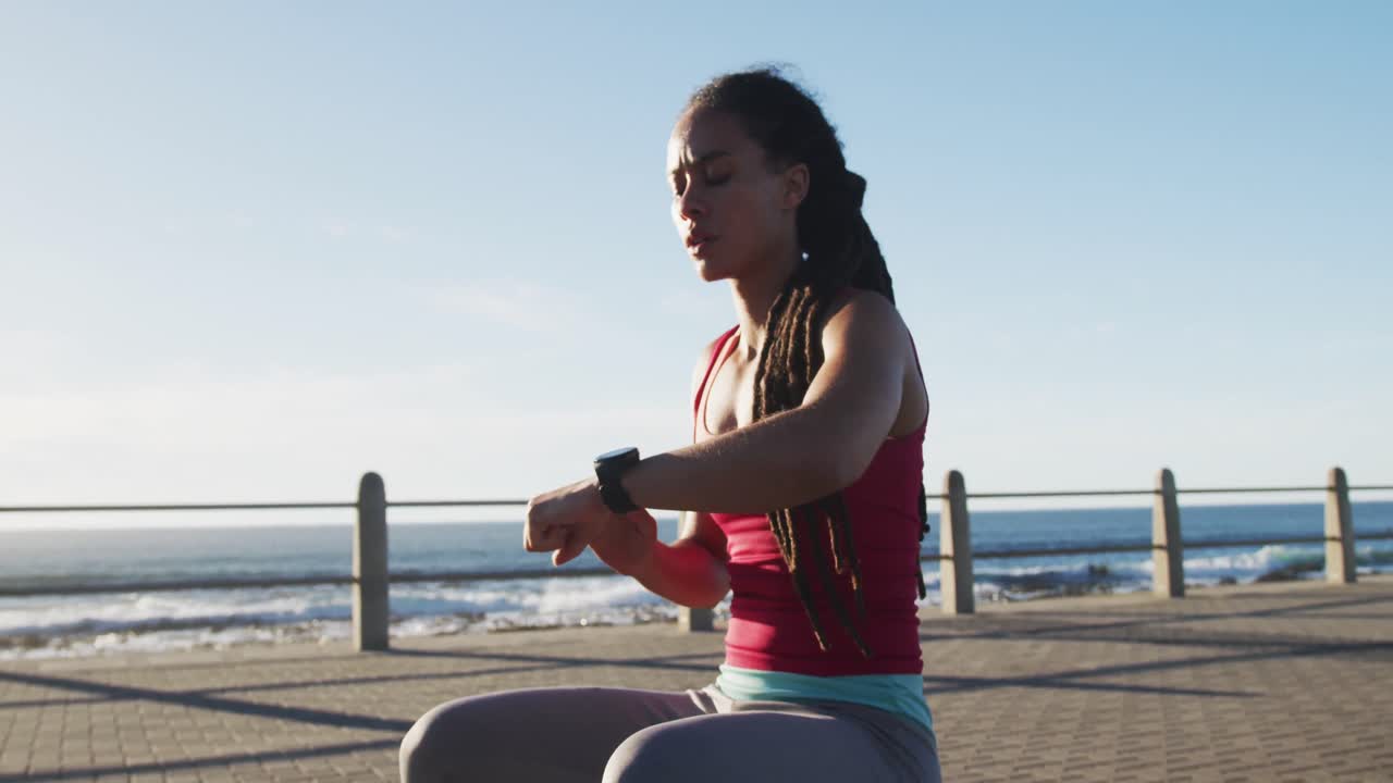 mujer afroamericana en ropa deportiva comprobando el reloj inteligente en el paseo marítimo