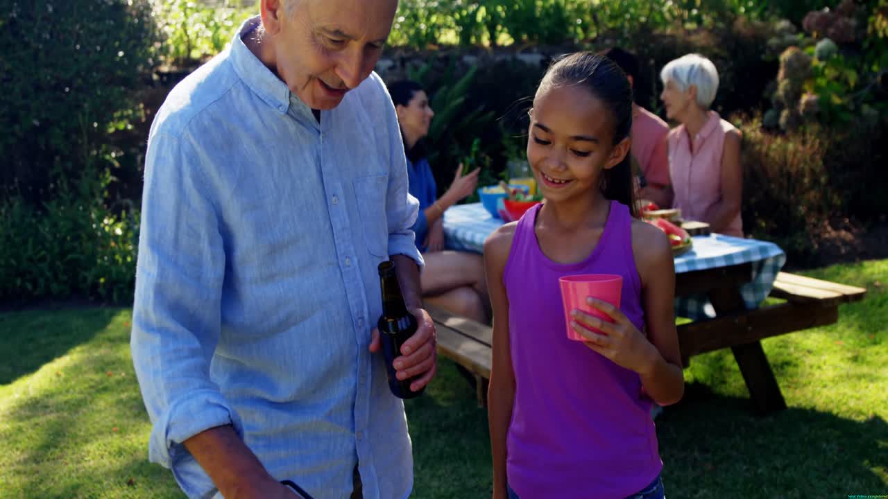 Grandfather and granddaughter preparing barbecue while family having meal 4k
