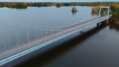 high angle aerial shot of a suspension bridge crossing a lake surrounded by an autumn forest with green, red, yellow and brown trees