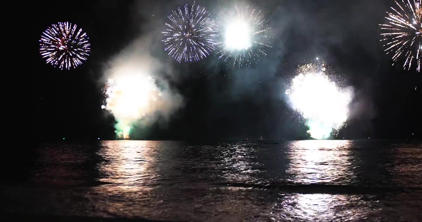 祝祭の夜、海上で打ち上げられる花火。色とりどりの花火が水面に映り込む。